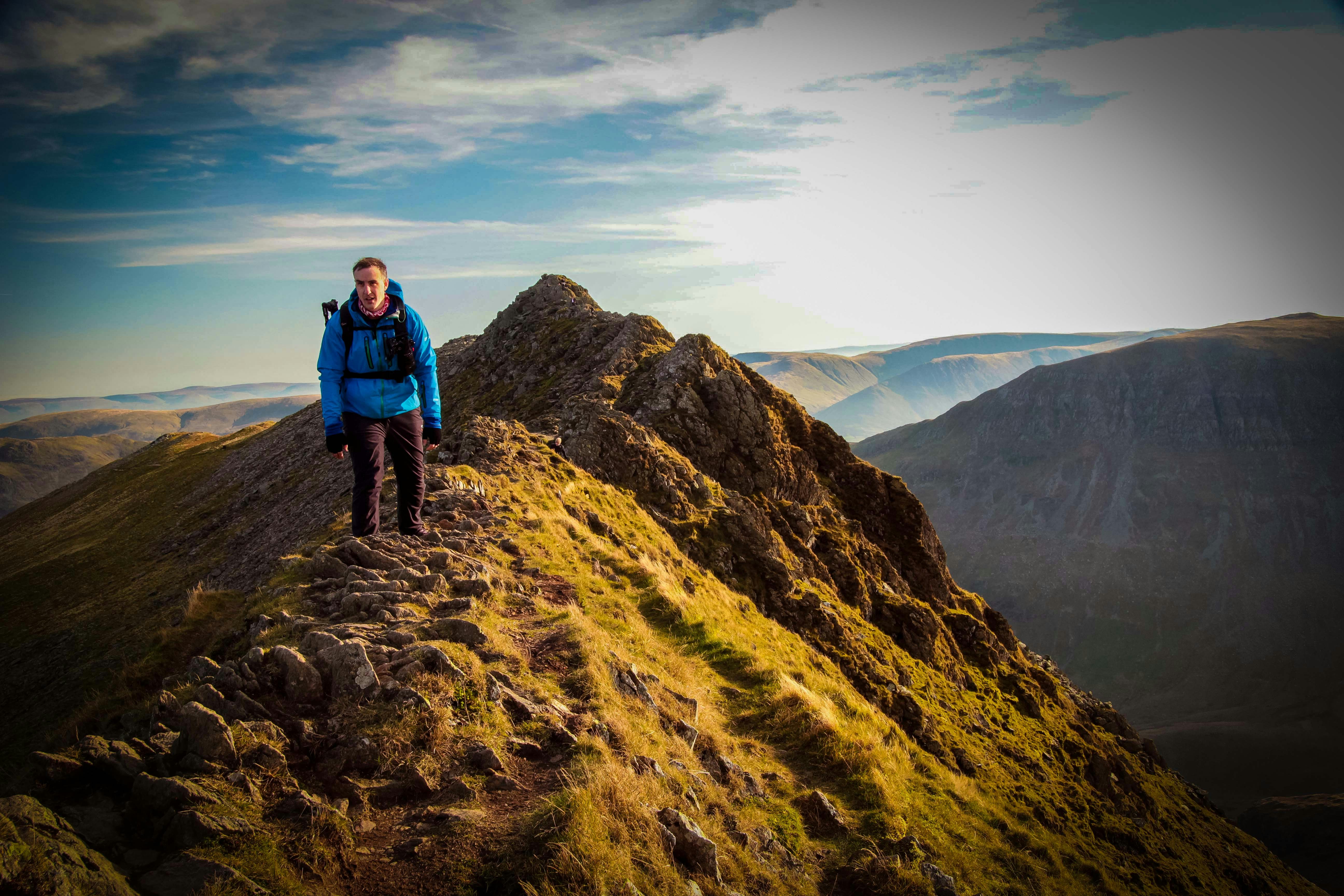 man in blue jacket and black pants standing on brown rocky mountain during daytime